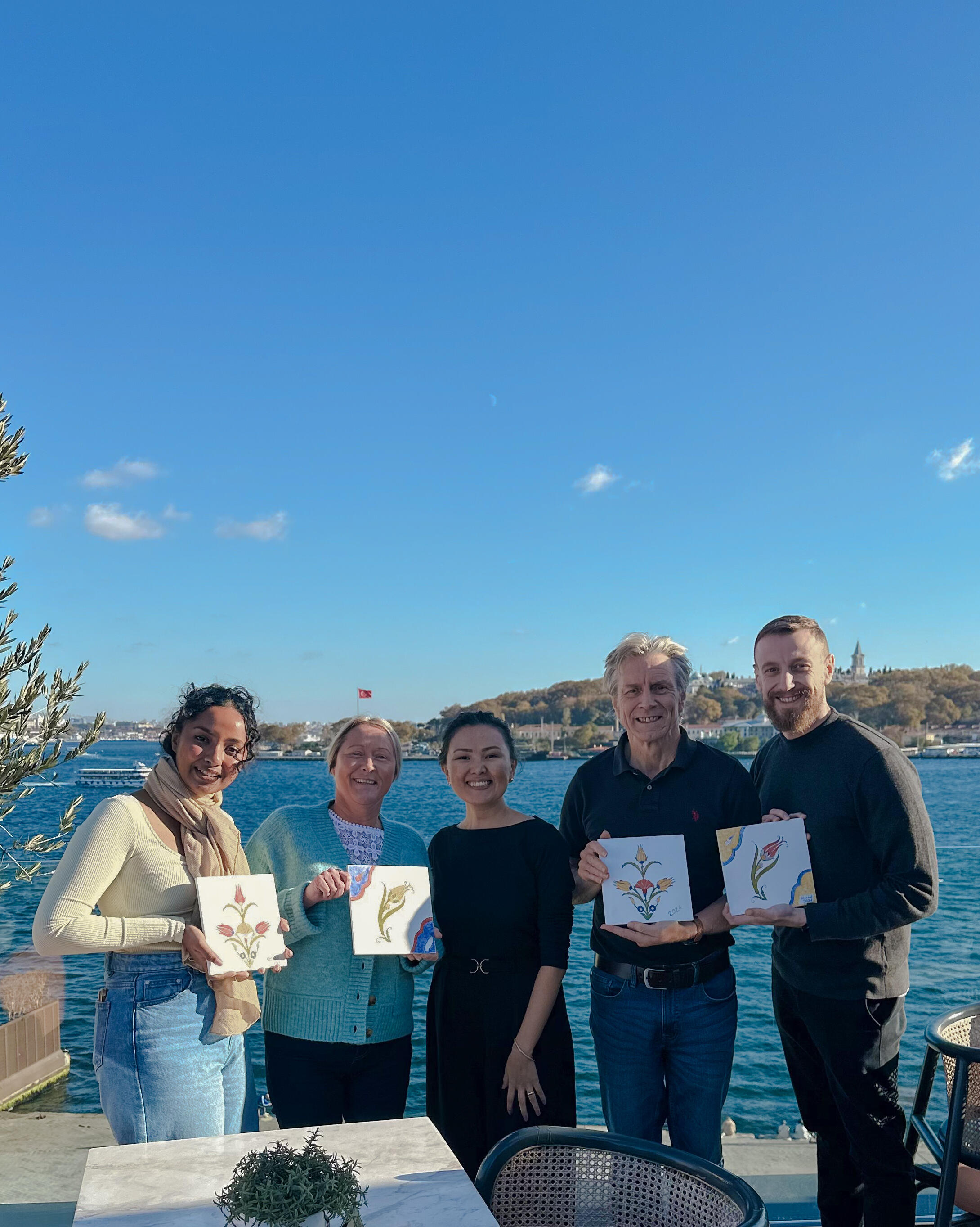 Group of people holding painted ceramic tiles, on the terrace of the hotel